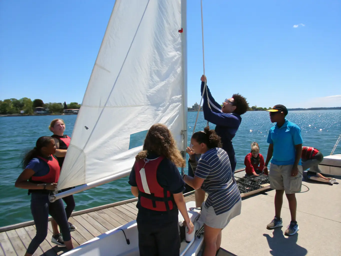 A group of children learning to sail small boats on a sunny day, with an instructor nearby, showcasing the introductory sailing program for kids.